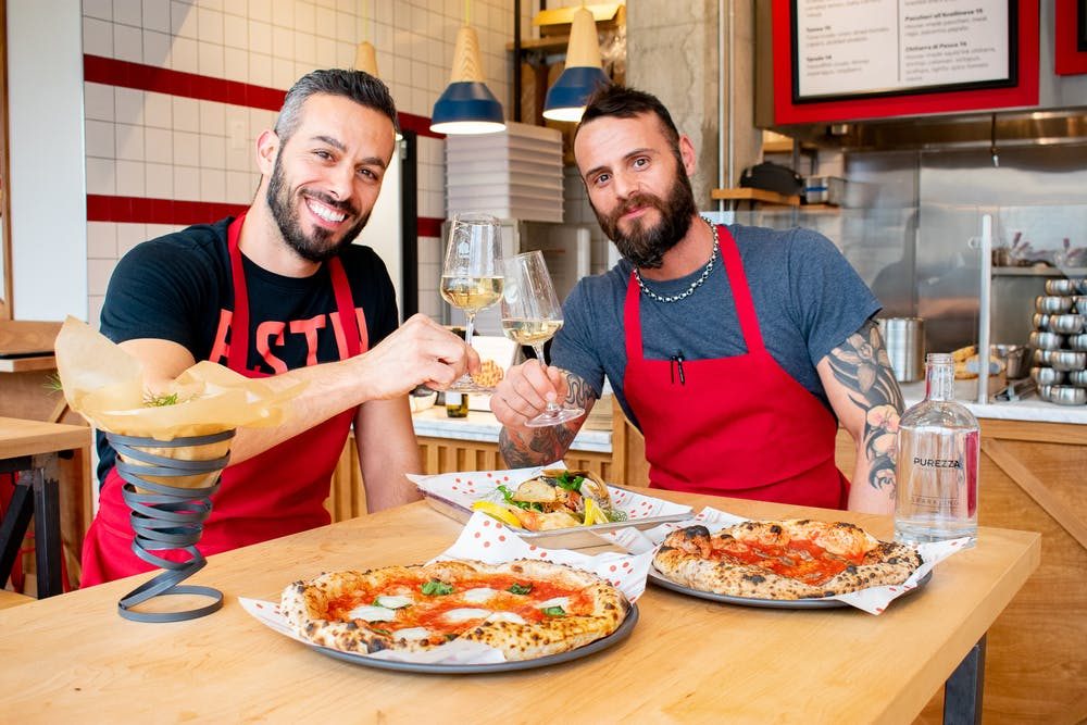 Two pizzaioli at the counter with fresh wood fired pizzas